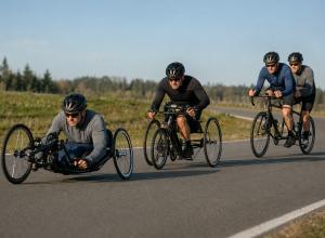 Trīs para riteņbraucēju ekipāžas ar rokas velosipēdu, triciklu un tandēmu brauc pa slēgtu šosejas trasi.
