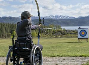 Para loka šāvējs sporta riteņkrēslā tēmē ar loku uz mērķi āra treniņu laukumā.