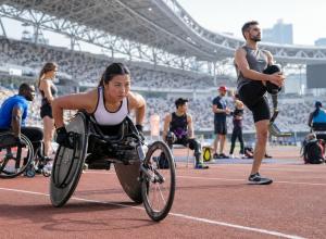 Para sportisti stadionā iesildās pirms sacensībām, tostarp sportiste sacensību riteņkrēslā