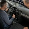 Cilvēks riteņkrēslā kopā ar tehniķi darbnīcā apskata automobilī uzstādītu rokas vadības ierīci.