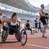 Para sportisti stadionā iesildās pirms sacensībām, tostarp sportiste sacensību riteņkrēslā