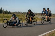 Trīs para riteņbraucēju ekipāžas ar rokas velosipēdu, triciklu un tandēmu brauc pa slēgtu šosejas trasi.