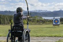 Para loka šāvējs sporta riteņkrēslā tēmē ar loku uz mērķi āra treniņu laukumā.