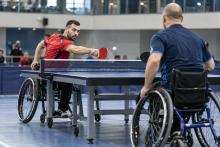 Divi para galda tenisisti riteņkrēslos izspēlē bumbiņu pie galda sporta hallē