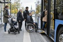 Riteņkrēsla lietotājs kopā ar citiem pasažieriem iekāpj zemās grīdas autobusā