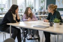 Skolniece riteņkrēslā kopā ar vecāku un skolotāju pārrunā mācību plānu klasē