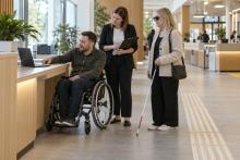 Cilvēki ar riteņkrēslu un balto spieķi kopā ar speciālisti pārbauda pašvaldības pakalpojumu