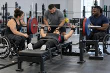 Para pauerliftinga sportiste izpilda spiešanu guļus, trenerim un komandas biedriem palīdzot