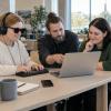 Trīs cilvēki bibliotēkā kopīgi pārbauda piekļūstamu digitālo pakalpojumu datorā un taktilā ierīcē