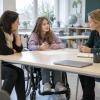Skolniece riteņkrēslā kopā ar vecāku un skolotāju pārrunā mācību plānu klasē