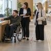 Cilvēki ar riteņkrēslu un balto spieķi kopā ar speciālisti pārbauda pašvaldības pakalpojumu