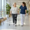 Paciente ar kruķiem fizioterapeites pavadībā iet pa gaišu rehabilitācijas centra gaiteni