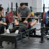 Para pauerliftinga sportiste izpilda spiešanu guļus, trenerim un komandas biedriem palīdzot